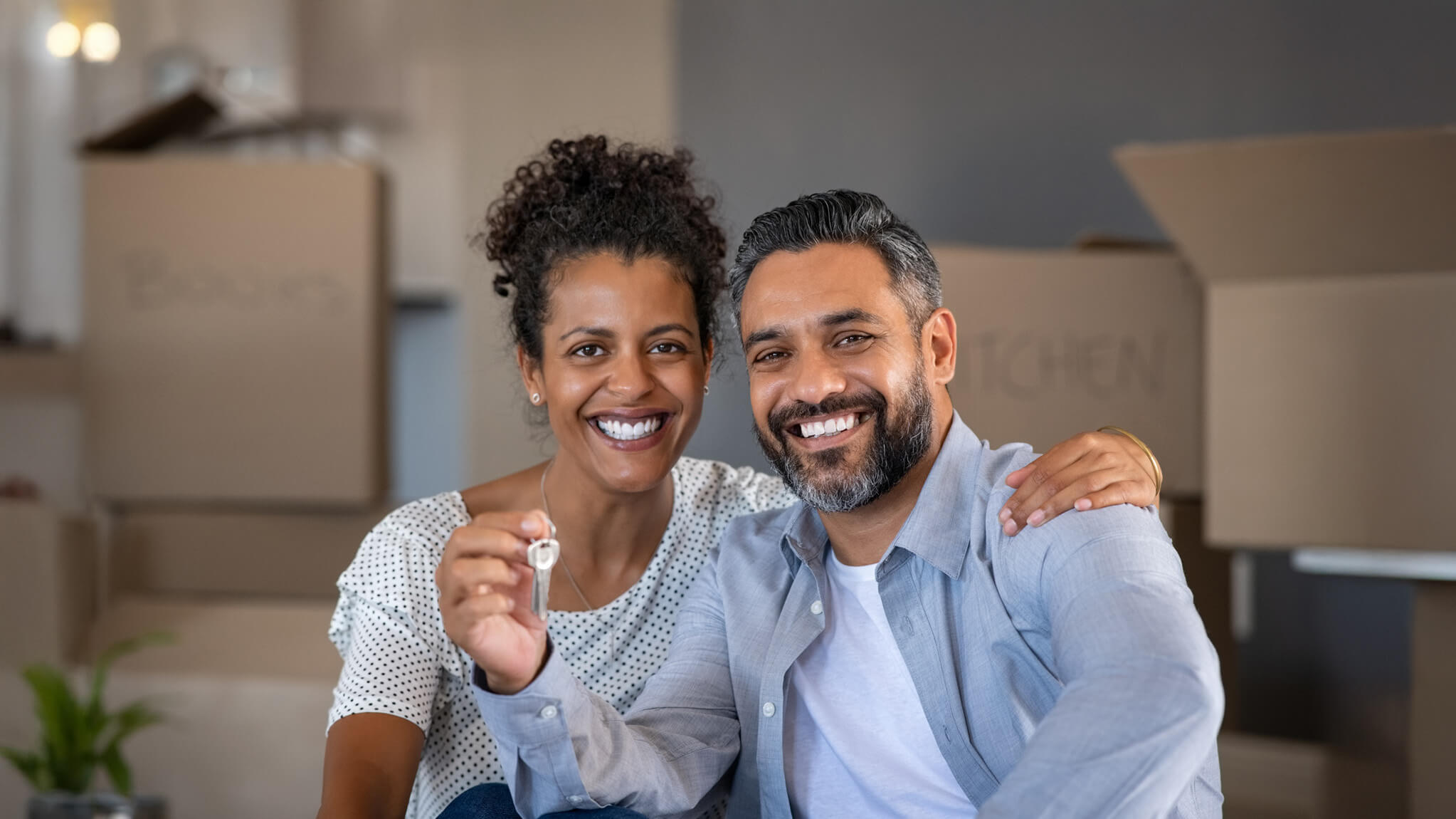 Couple holding up key to new house with packing boxes in background